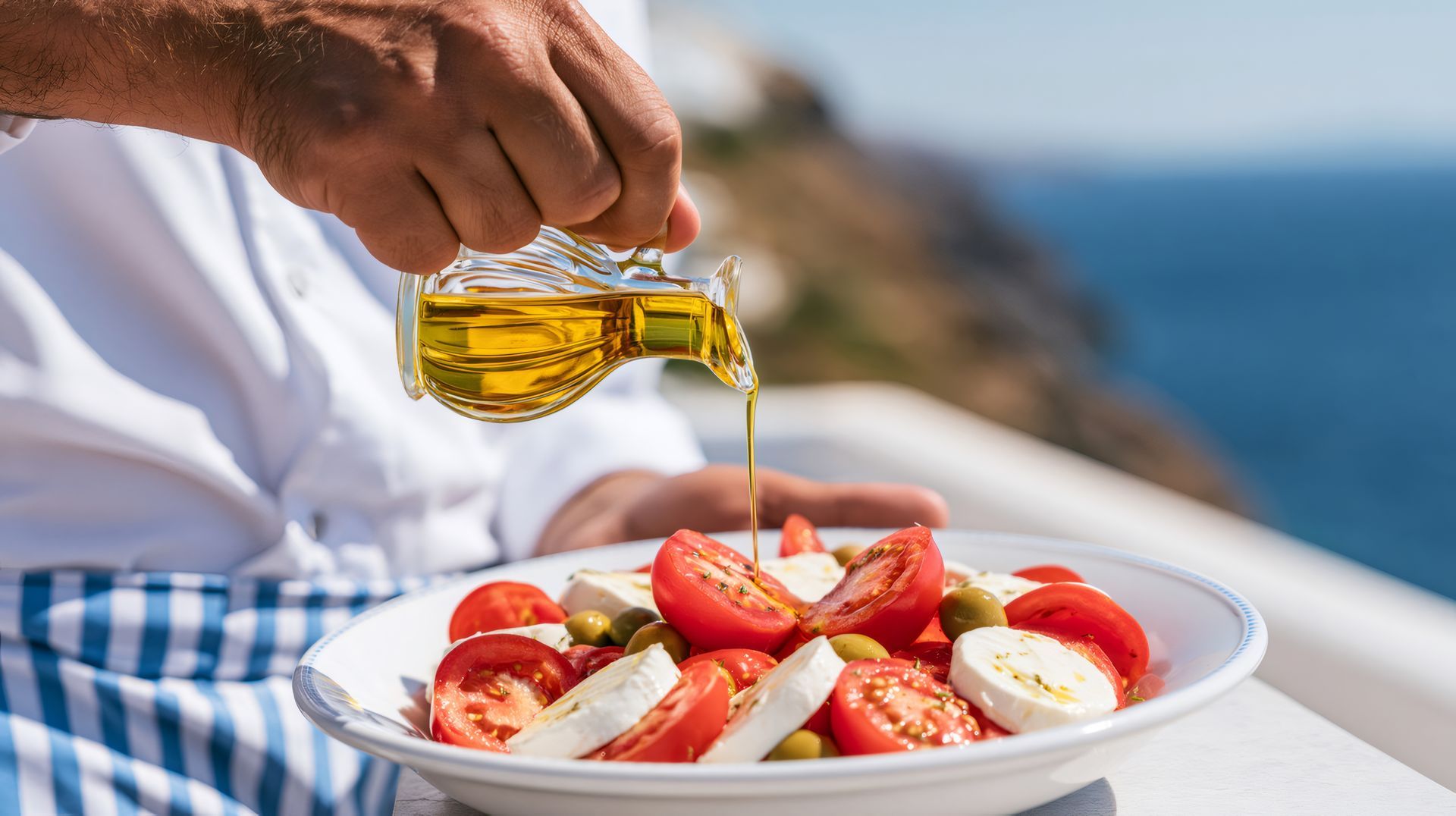 Une main verse de l'huile d'olive sur une salade de tomates et de fromage au bord de la mer
