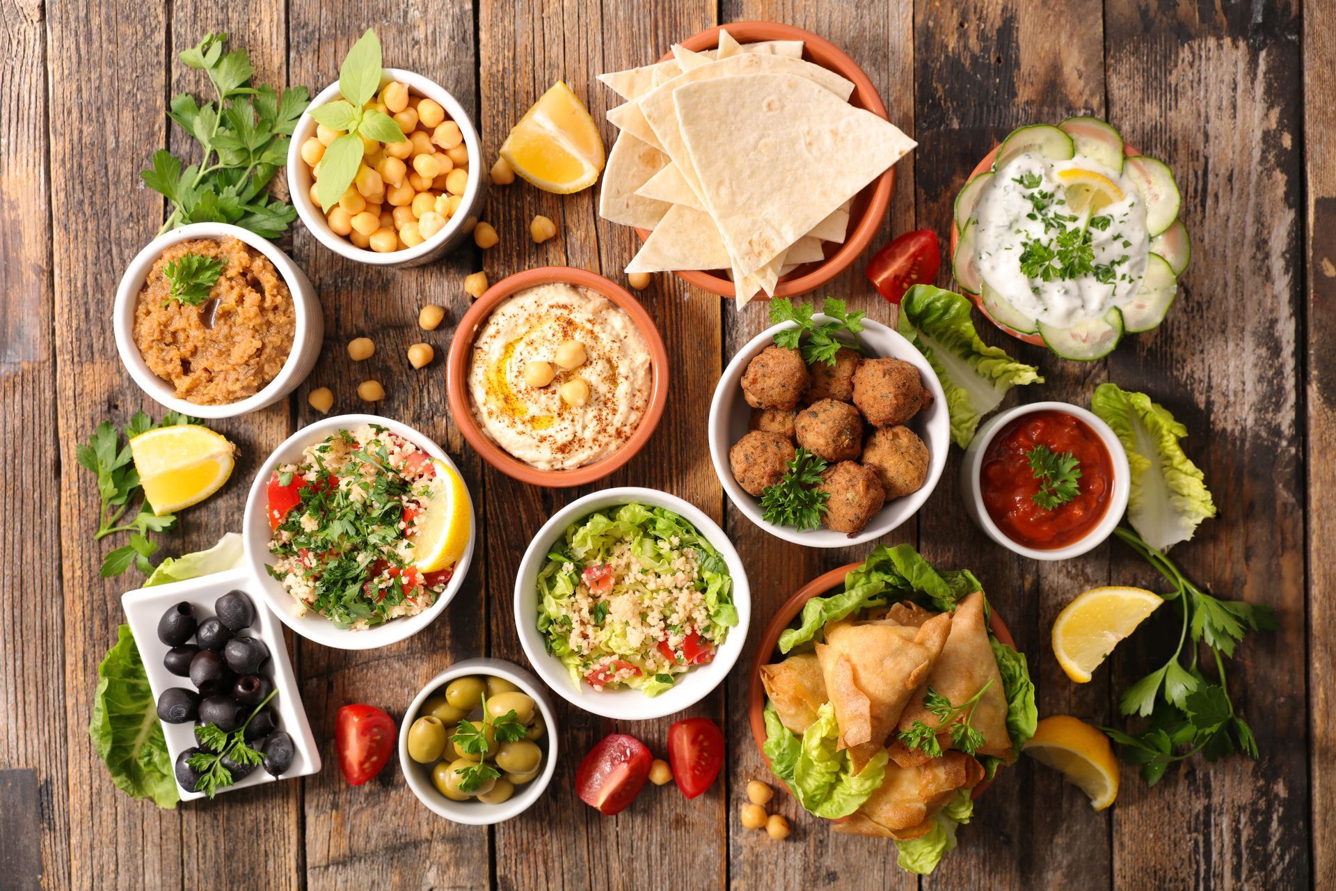 Assortiment de mezzés du Moyen-Orient disposés sur une table rustique en bois, avec du pain pita, des sauces, des olives et des falafels