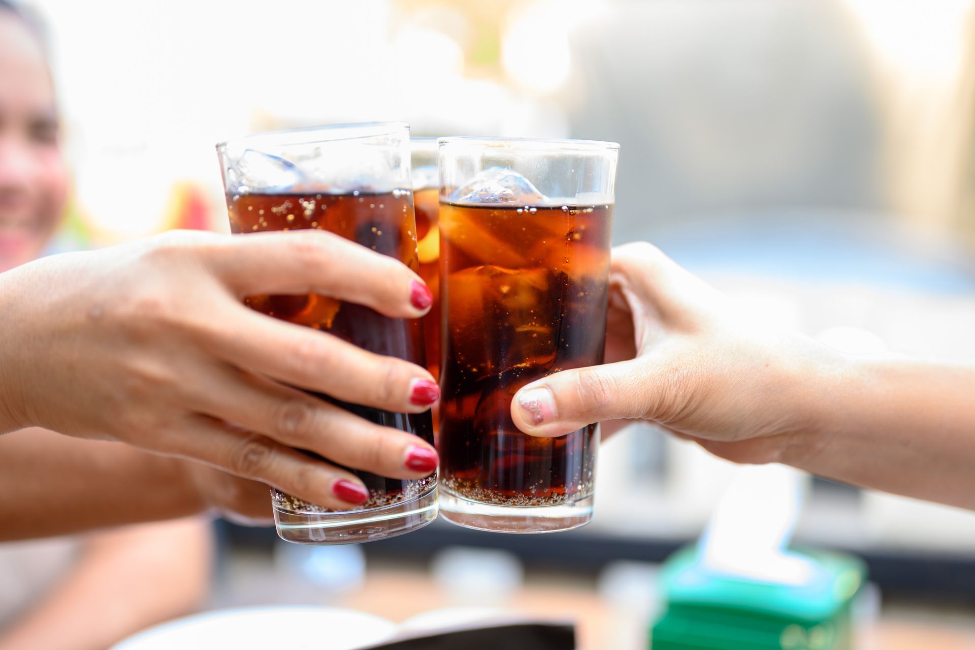 Deux mains qui trinquent avec des verres de soda foncé et de glace à une table ensoleillée en terrasse
