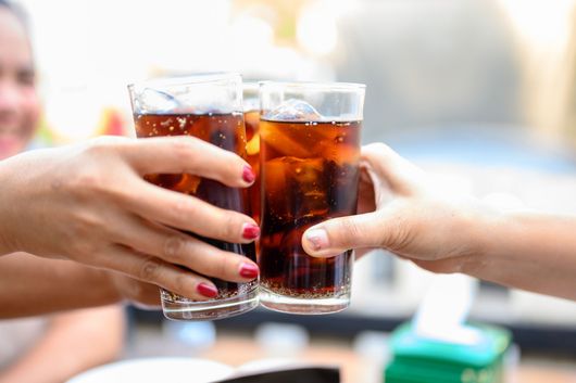 Deux mains trinquent avec des verres de cola glacé à la paille dans un cadre lumineux et décontracté