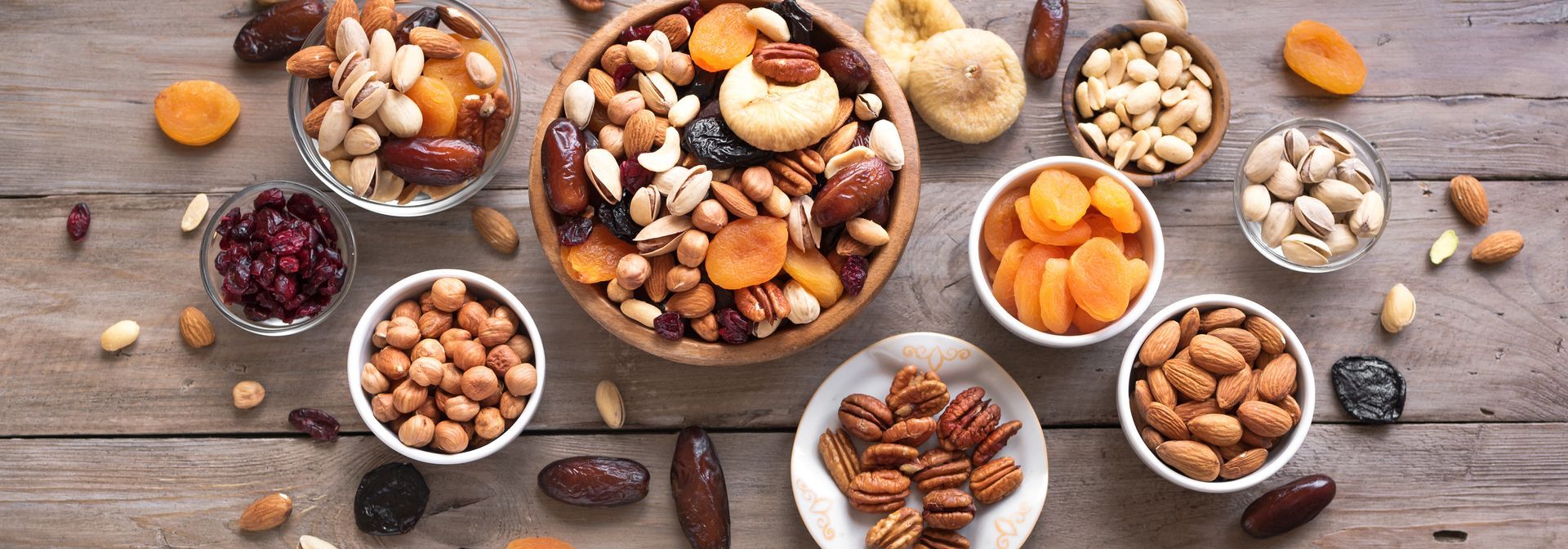 Assortiment de noix et de fruits secs dans des bols blancs sur une table rustique en bois, vue de dessus