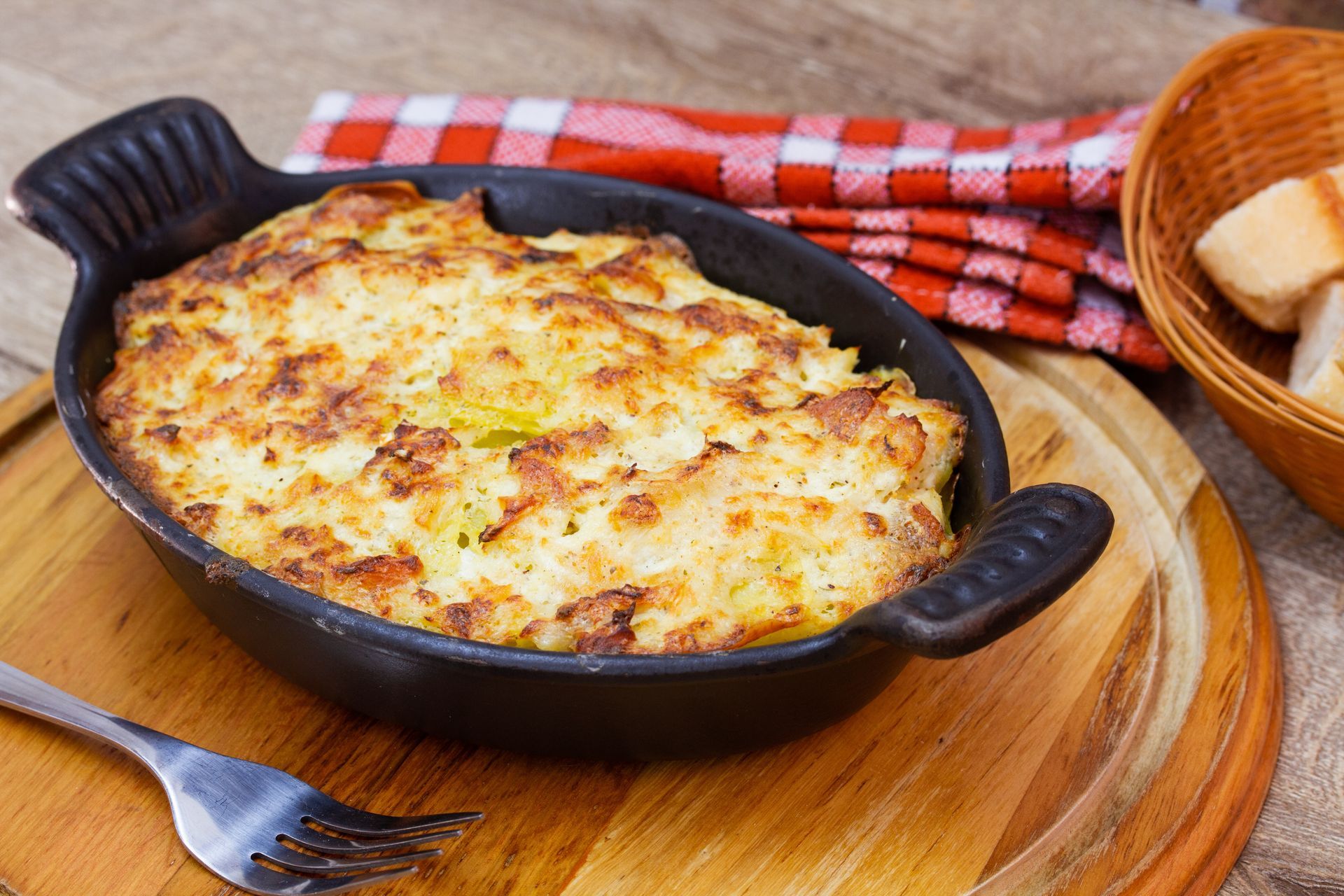 Gratin de fromage cuit au four dans une poêle noire, servi sur une planche en bois avec du pain.