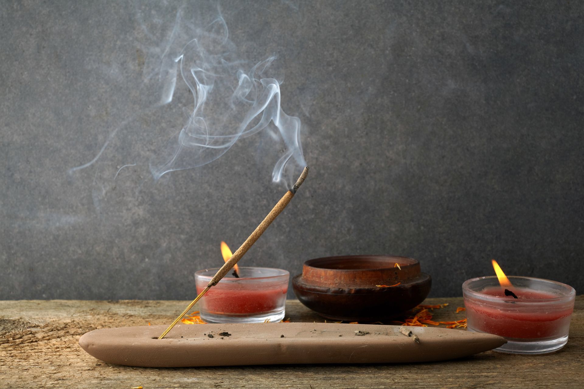 Encens allumé, bougies et bol sur un plateau en bois, le tout sur fond sombre.