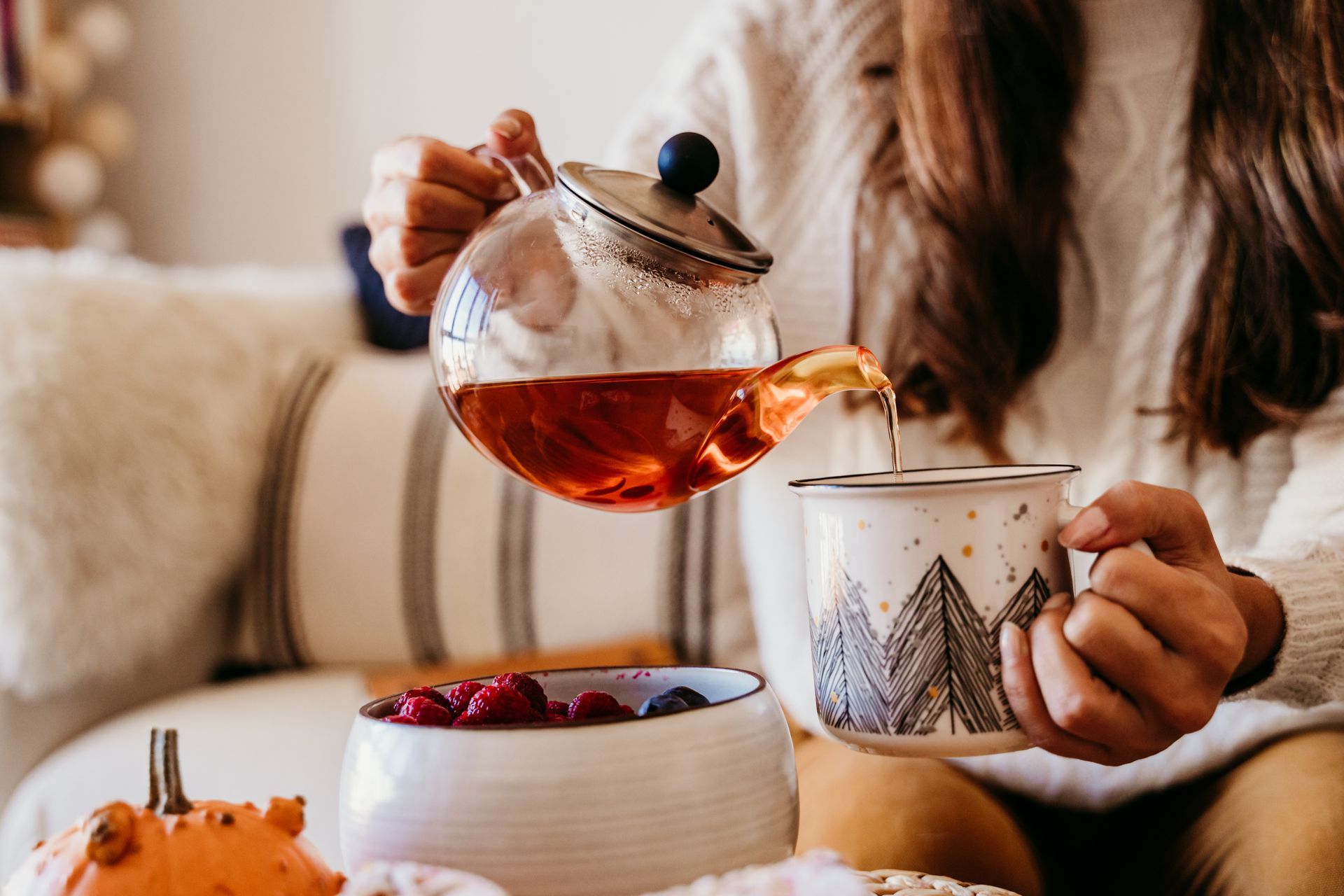 Verser du thé à la main d'une théière en verre dans une tasse à côté d'un bol de baies sur une table accueillante