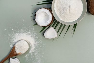 Moitiés de noix de coco et farine de noix de coco dans des bols avec une cuillère en bois sur un fond vert pâle
