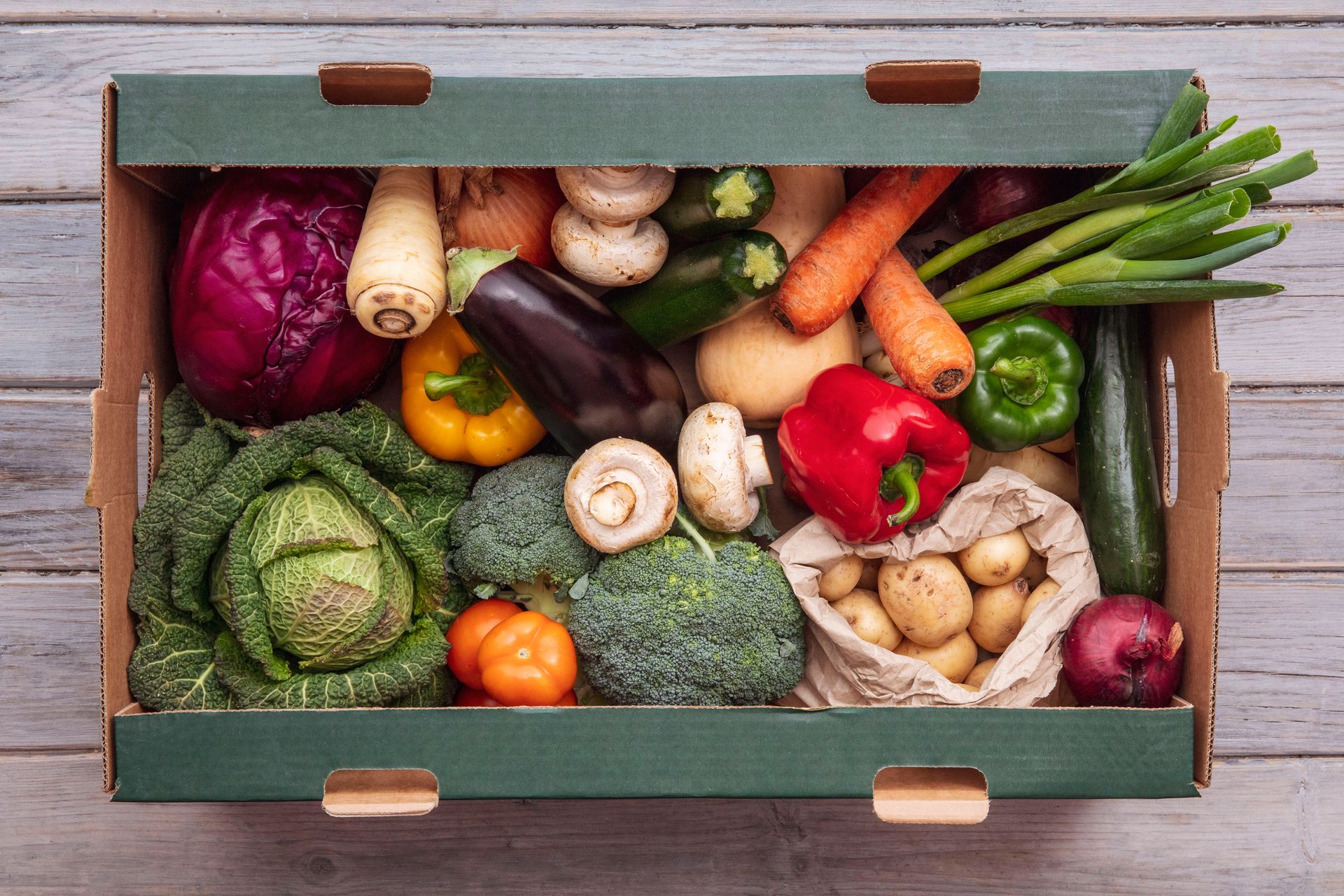 Caisse de légumes frais assortis, comprenant brocolis, poivrons, carottes et champignons, sur une table en bois
