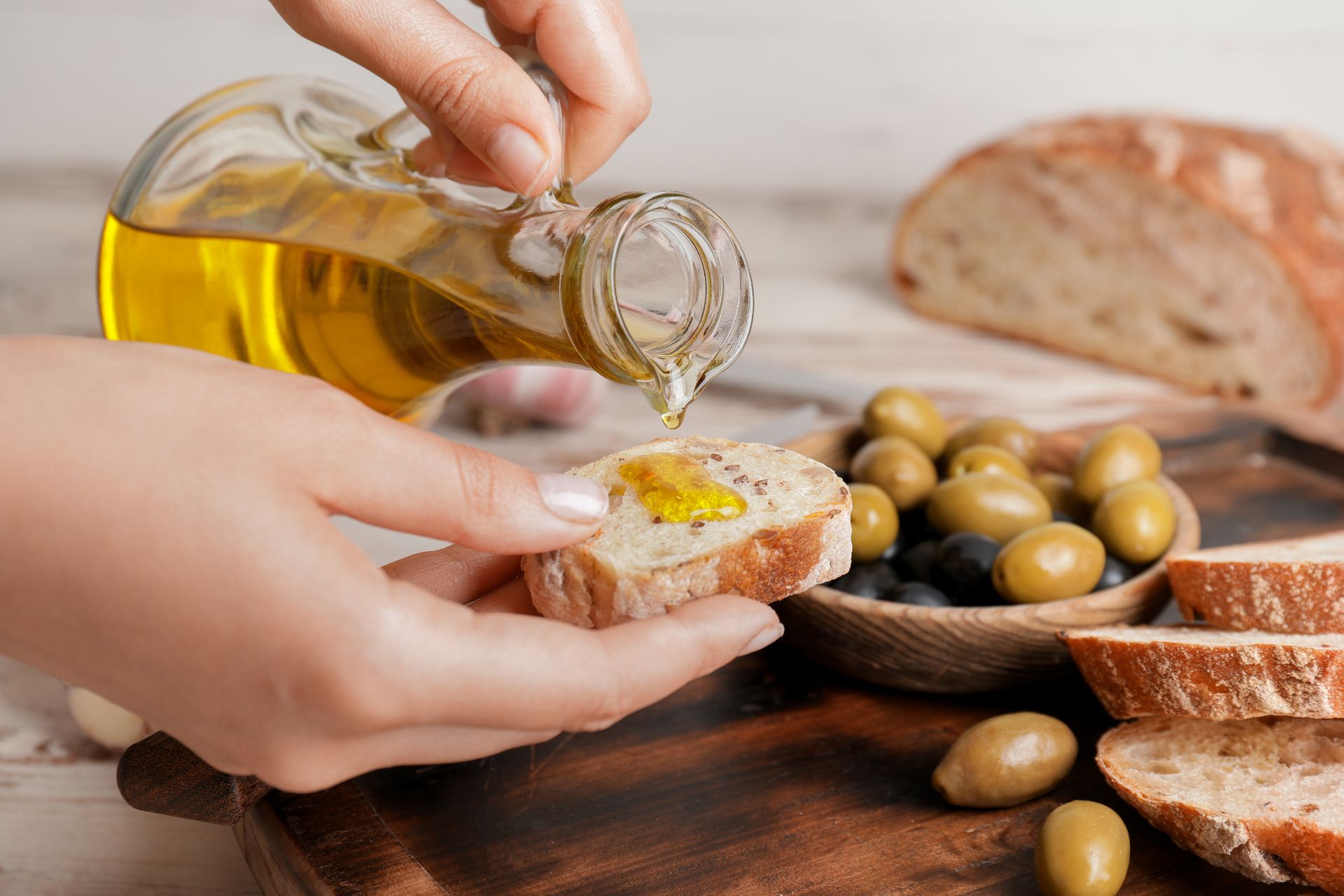Huile d'olive versée sur du pain avec des olives et du pain tranché sur une table en bois