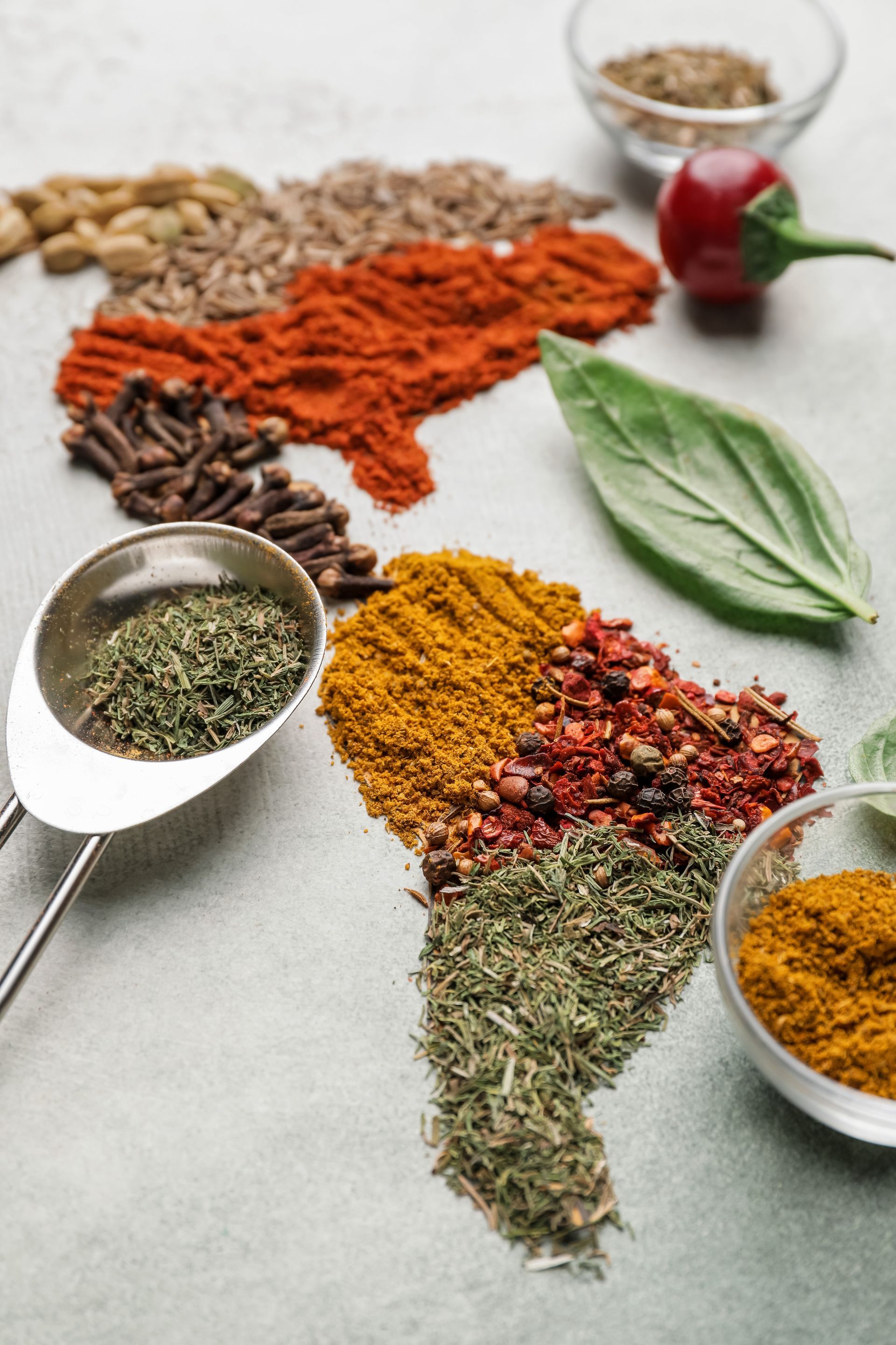 Assortiment d'épices et d'herbes colorées disposées sur une surface blanche avec des bols et des feuilles fraîches