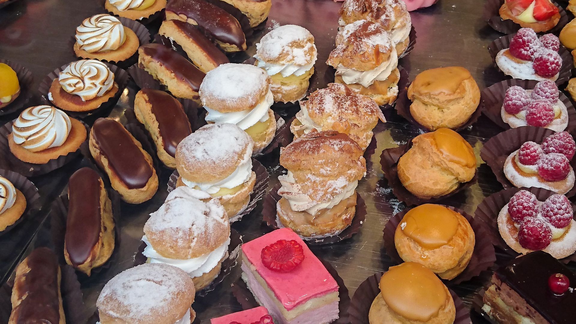 Assortiment de pâtisseries et tartes colorées disposées en rangées sur une vitrine de boulangerie.