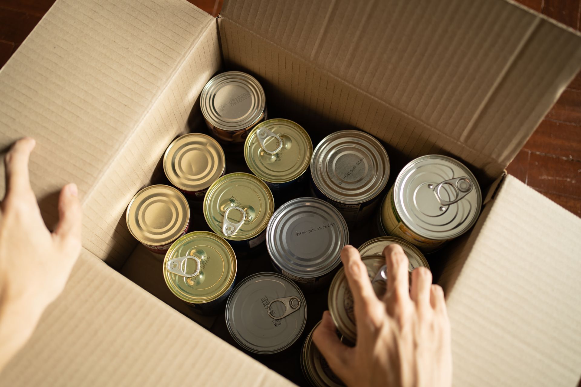 Des mains emballent des conserves assorties dans une boîte en carton