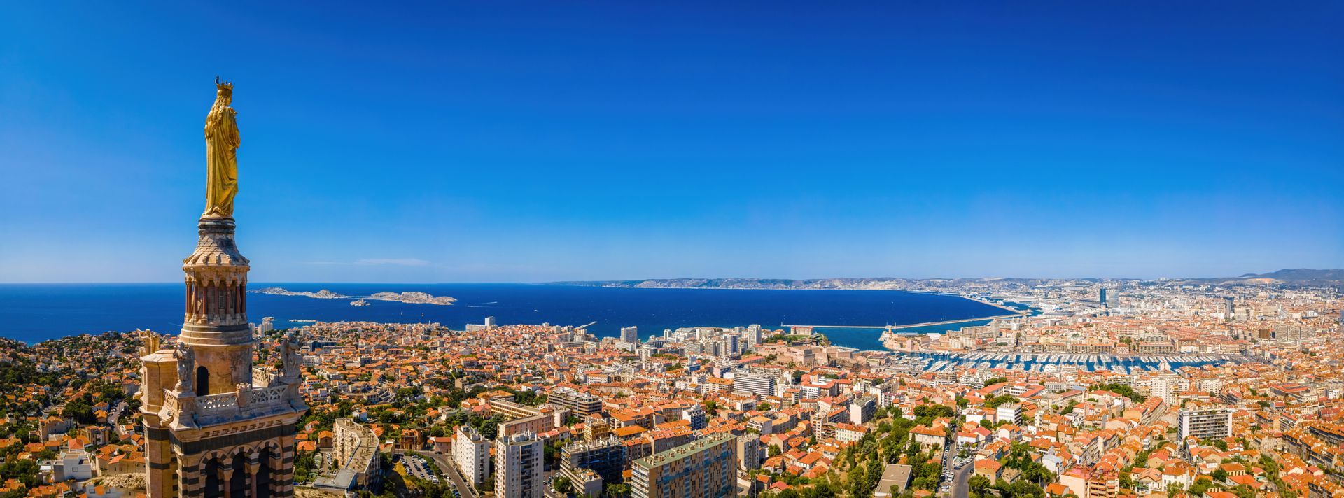 Vue panoramique d'un paysage urbain avec une haute statue au premier plan et une mer bleue sous un ciel dégagé.