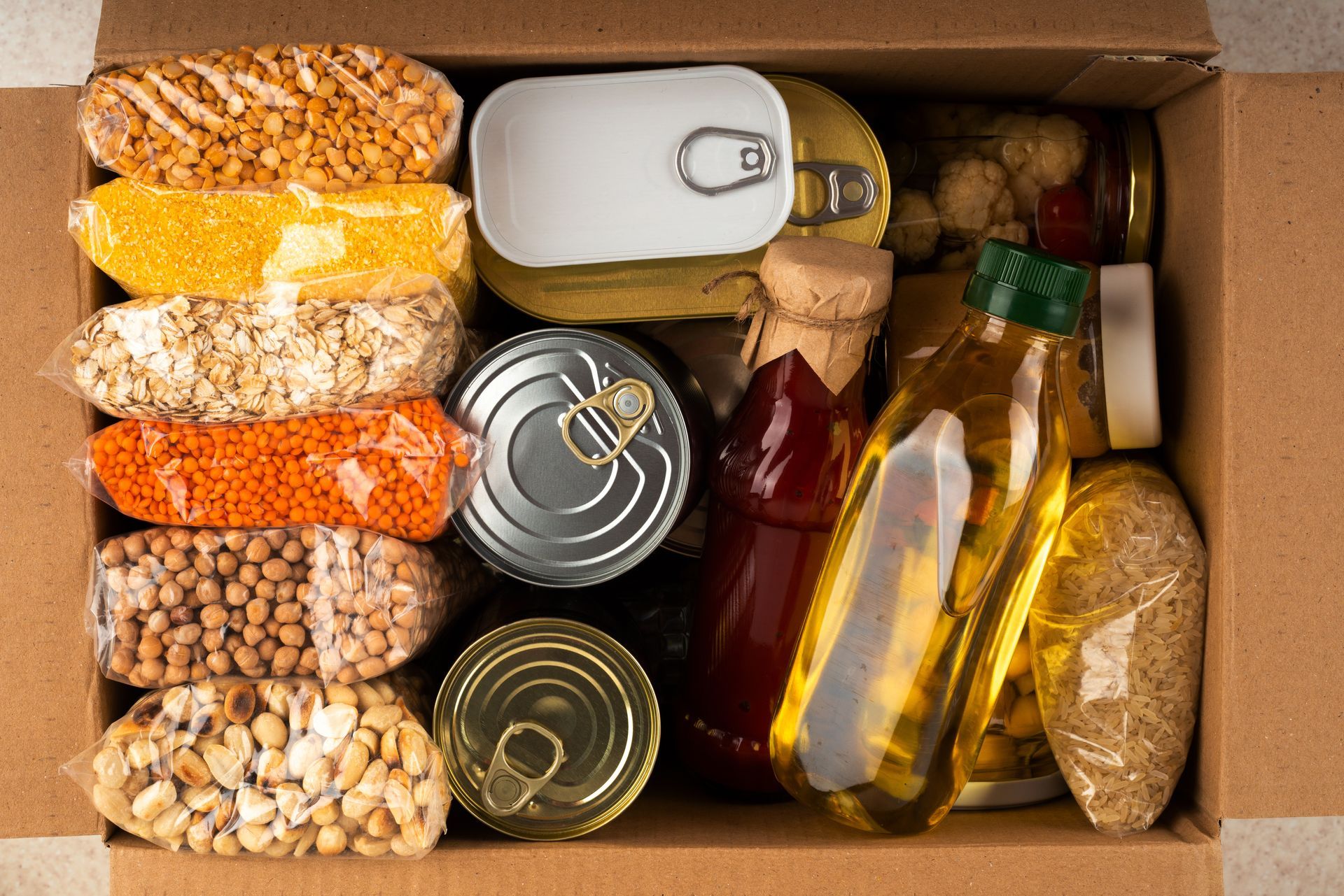 Boîte de provisions alimentaires emballées et en conserve assorties, comprenant des céréales, des pâtes et des bouteilles d'huile