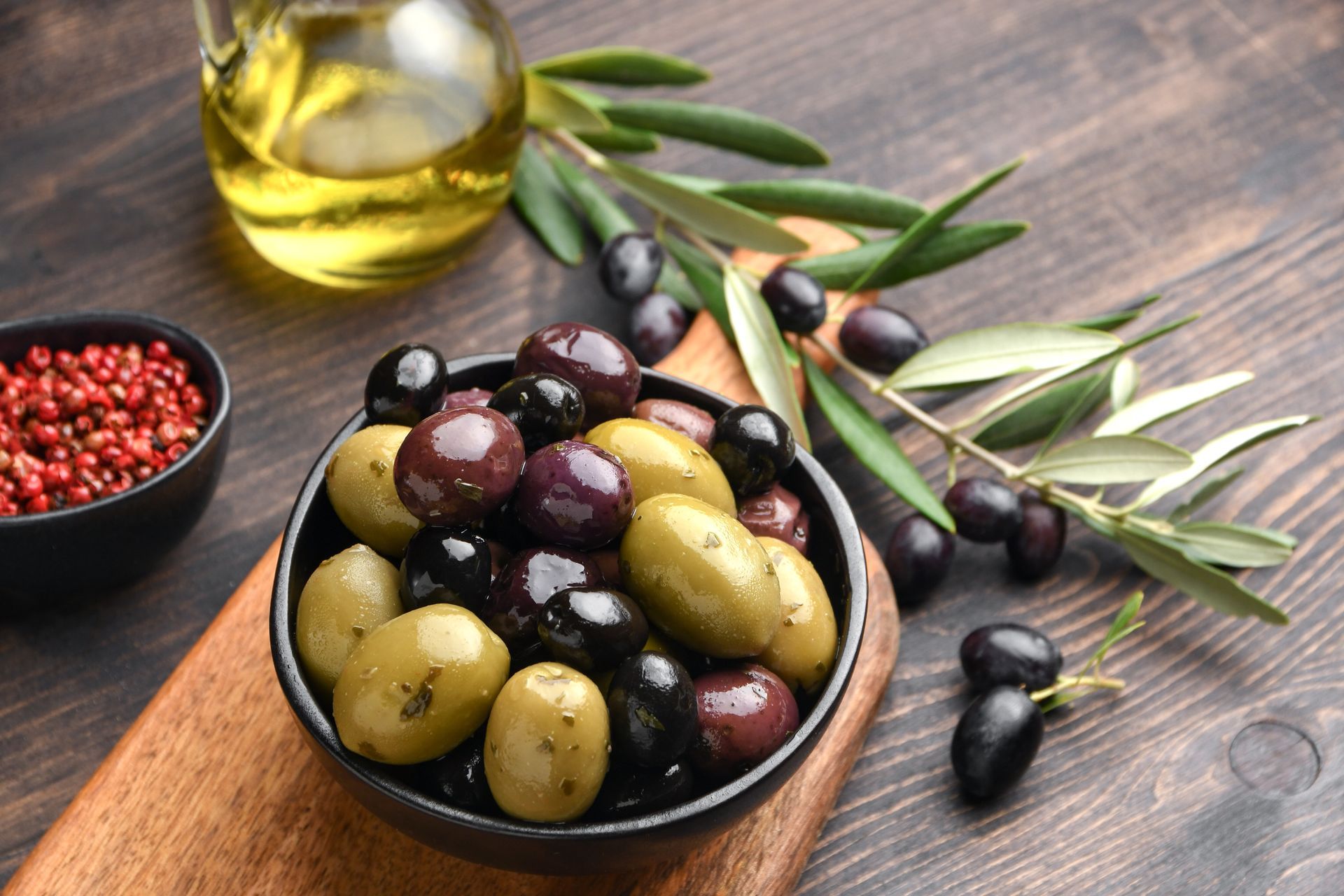 Bol d'olives mélangées avec de l'huile d'olive et olives sur des branches sur une table en bois