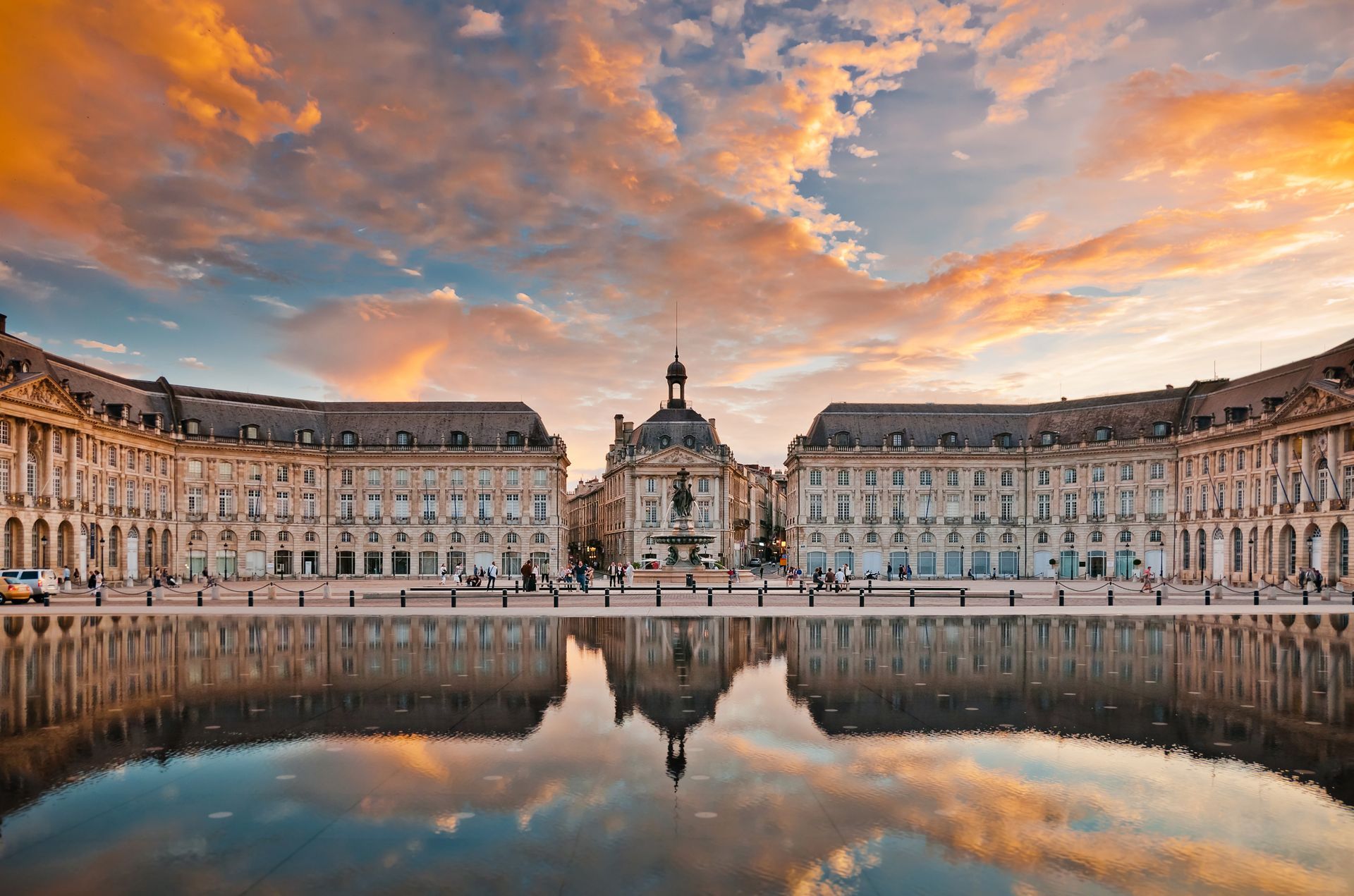 Cour du grand palais au coucher du soleil, avec des nuages ​​orangés se reflétant dans le bassin immobile d'une fontaine.
