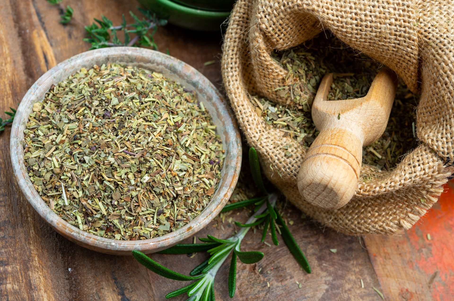 Des herbes séchées dans un bol à côté d'un pilon en bois et d'un sac de jute sur une table rustique