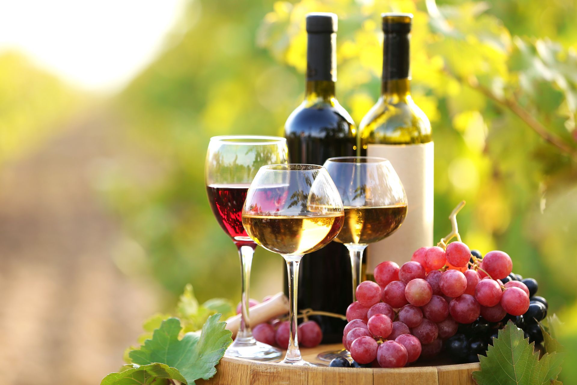 Verres à vin, bouteilles et raisins rouges sur une table en bois dans un vignoble ensoleillé