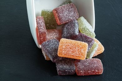 Des bonbons gélifiés colorés enrobés de sucre se sont renversés d'un récipient blanc sur une surface sombre.