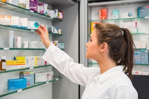 Una farmacéutica está mirando una caja de pastillas en una farmacia.