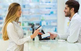Una mujer le está dando una tarjeta de crédito a un farmacéutico en una farmacia.