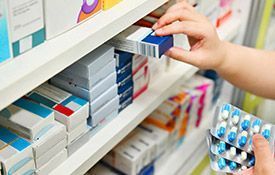 Una persona está recogiendo una caja de pastillas de un estante de una farmacia.