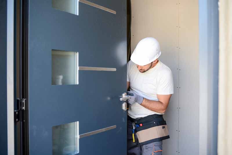 Ouvrier portant un casque de chantier installant des ferrures sur un cadre de porte bleu à l'intérieur.