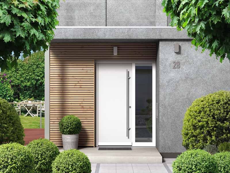 Entrée d'une maison moderne avec porte blanche, bardage en bois et arbustes taillés dans un jardin.