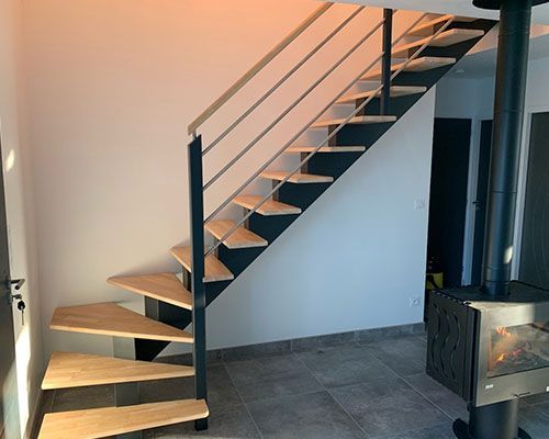 Escalier intérieur moderne avec marches en bois, rampes noires et un petit poêle à bois à proximité