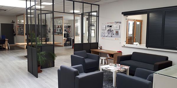 Salon de bureau moderne avec chaises noires, cloisons en verre et petite table avec magazines