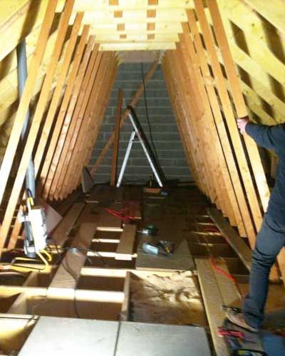 Intérieur d'un grenier en bois en cours d'aménagement, avec charpente, outils et un ouvrier sur la droite.