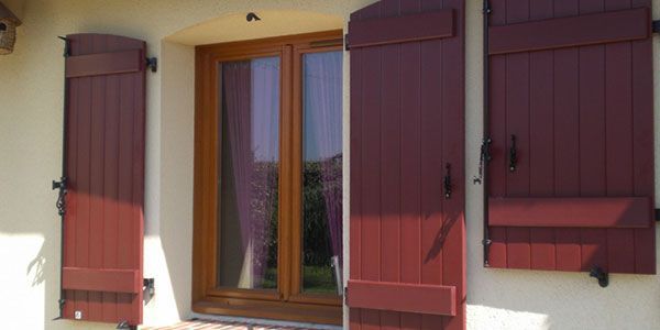Fenêtre de maison avec volets marron et petite jardinière sur un mur crème
