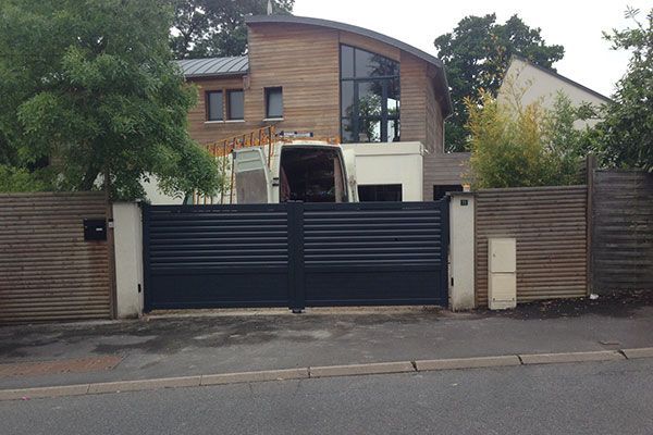 Maison moderne derrière un portail noir et un mur de briques dans une rue calme