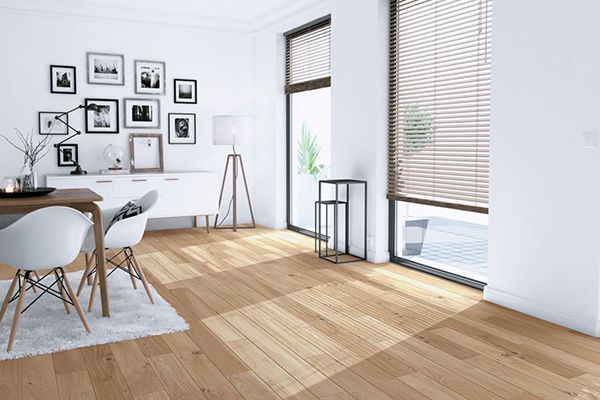 Salle à manger moderne et lumineuse avec parquet, chaises blanches, mur de cadres et grandes fenêtres avec stores.