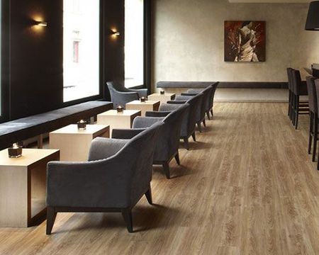 Salon d'hôtel moderne avec fauteuils gris, petites tables, parquet et éclairage mural tamisé