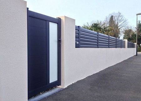 Mur blanc moderne et portail sombre le long d'une rue pavée par temps clair