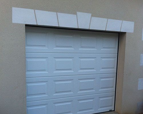 Porte de garage blanche sur un mur beige avec moulures décoratives au-dessus.