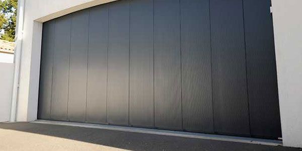 Grande porte de garage coulissante noire sur un mur extérieur blanc moderne
