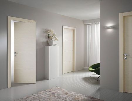 Chambre moderne et lumineuse avec portes ouvertes couleur crème, armoire blanche et chaise verte près de voilages.