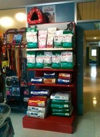 Alimentos y suministros para mascotas en un estante rojo de una tienda.