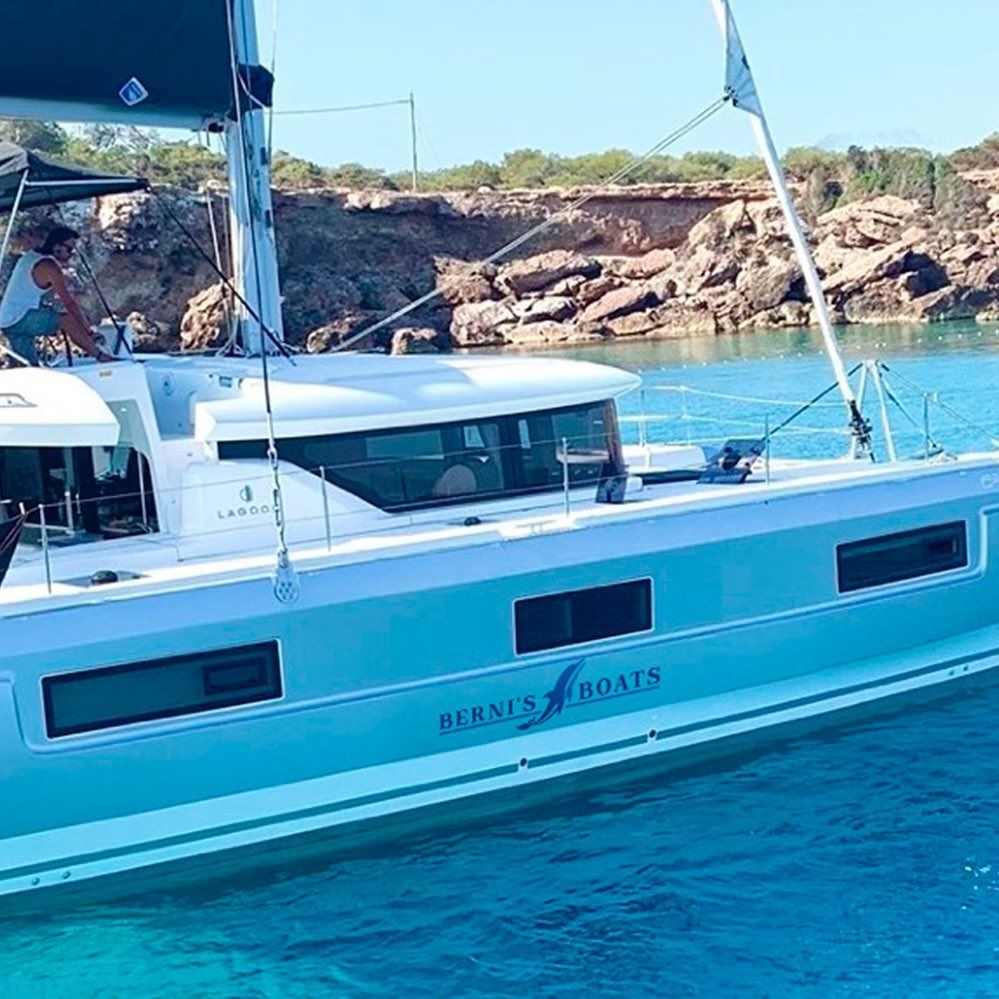 Catamarán navegando cerca de una costa rocosa. Aguas turquesas. Logotipo de 