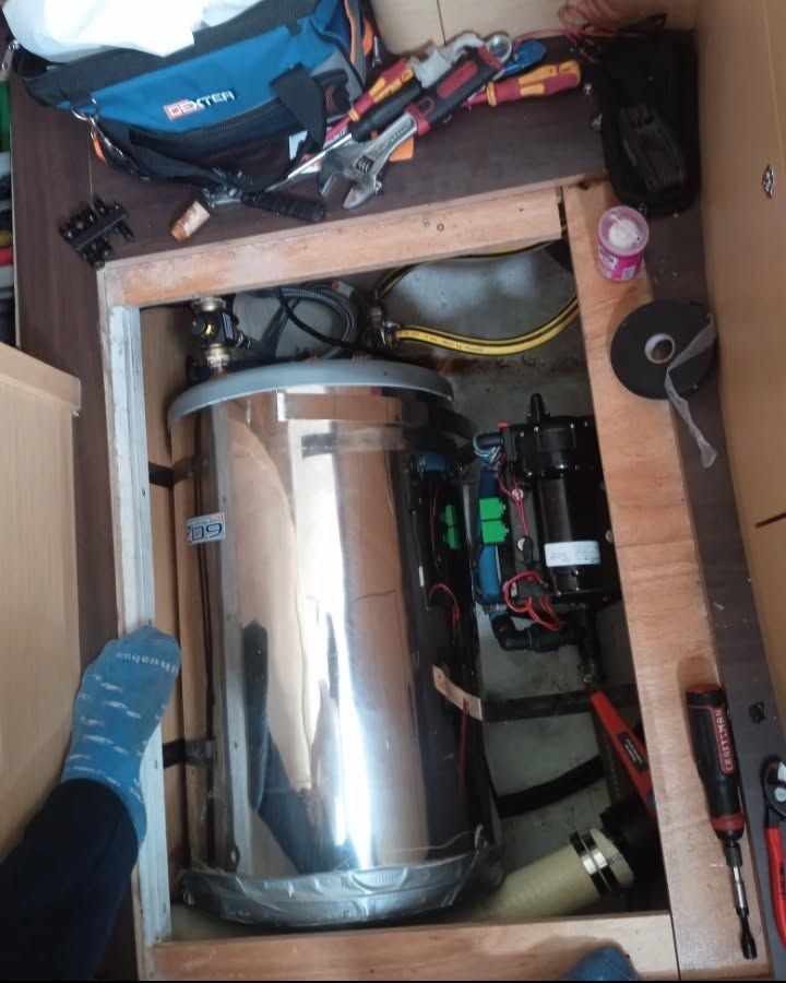 Calentador de agua y bomba instalados dentro de un gabinete de madera con herramientas y componentes eléctricos.