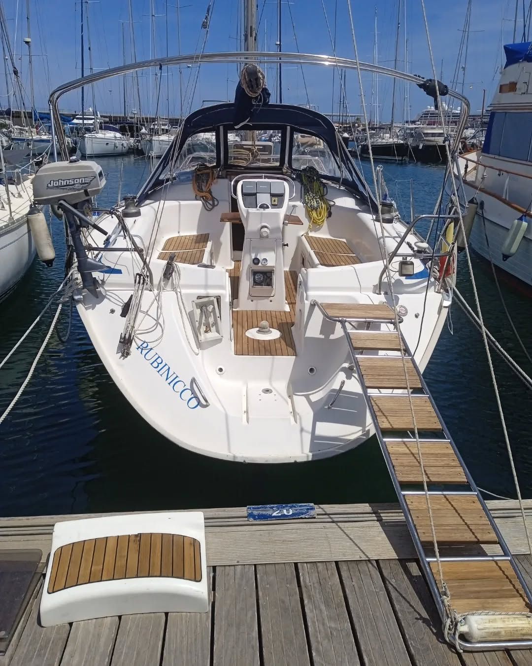 Velero blanco atracado en puerto deportivo con pasarela de madera.