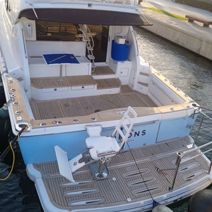 Vista trasera de un barco azul y blanco con cubiertas de madera y una silla de pesca.