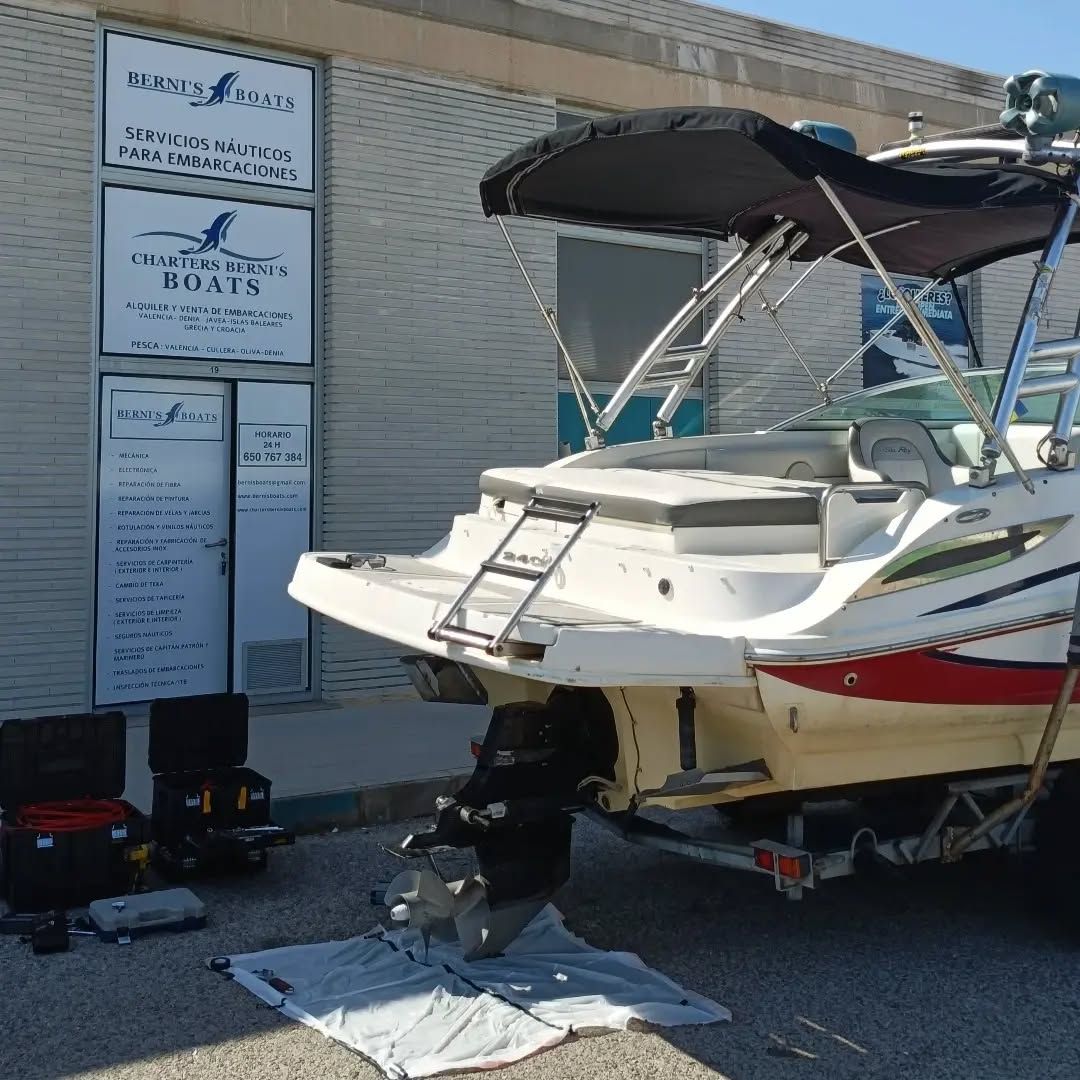 Barco estacionado afuera de un taller de reparación de barcos con herramientas y equipos visibles.
