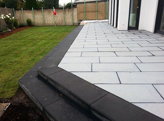 Eine Terrasse mit hinaufführenden Stufen und einem Rasen im Hintergrund.