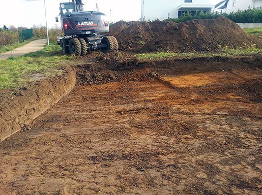 Ein Bulldozer gräbt ein Loch in die Erde vor einem Haus.