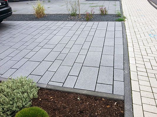 Auf einer gepflasterten Auffahrt neben einem Busch ist ein Auto geparkt.