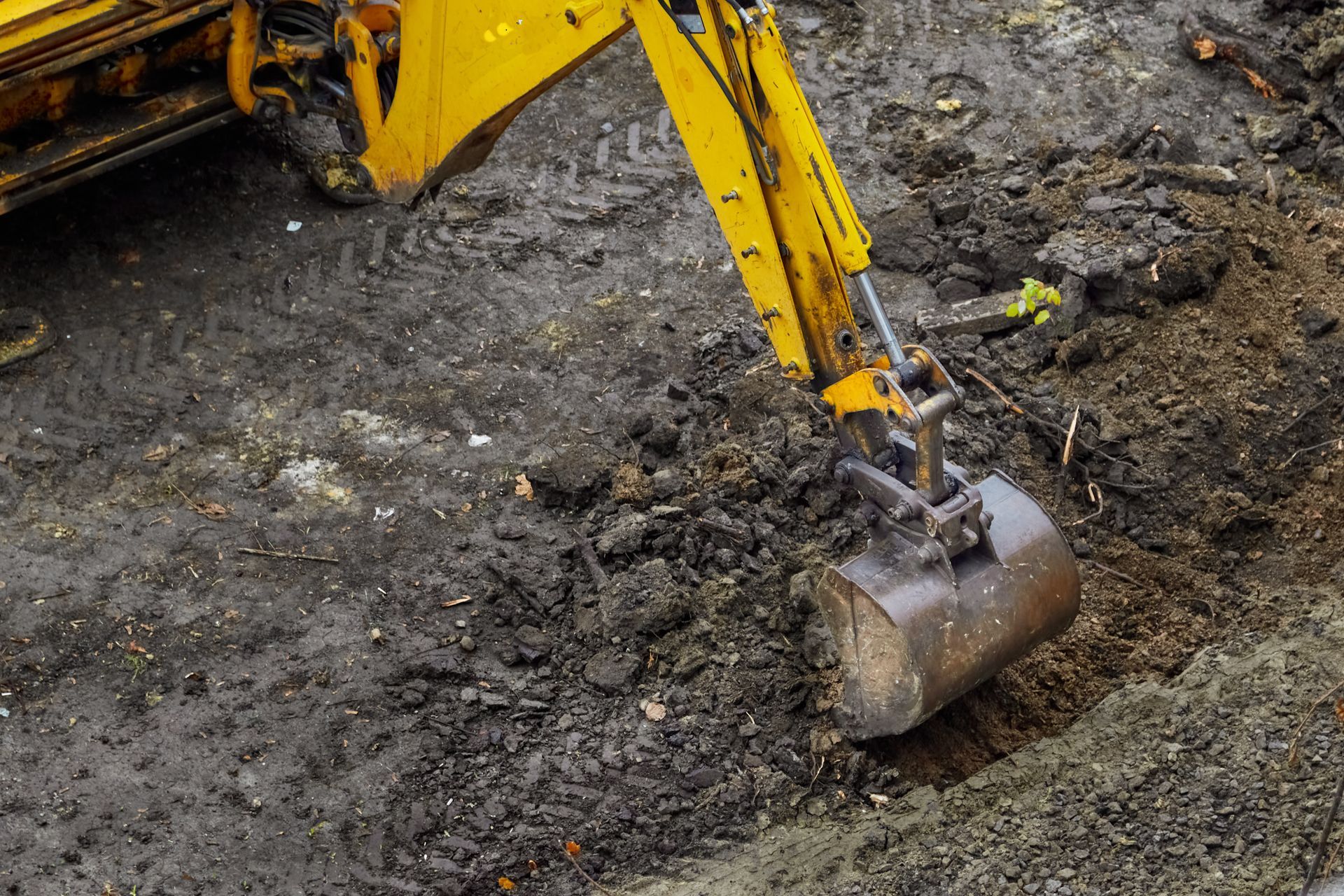 Un godet de pelleteuse jaune creuse dans un sol boueux sur un chantier