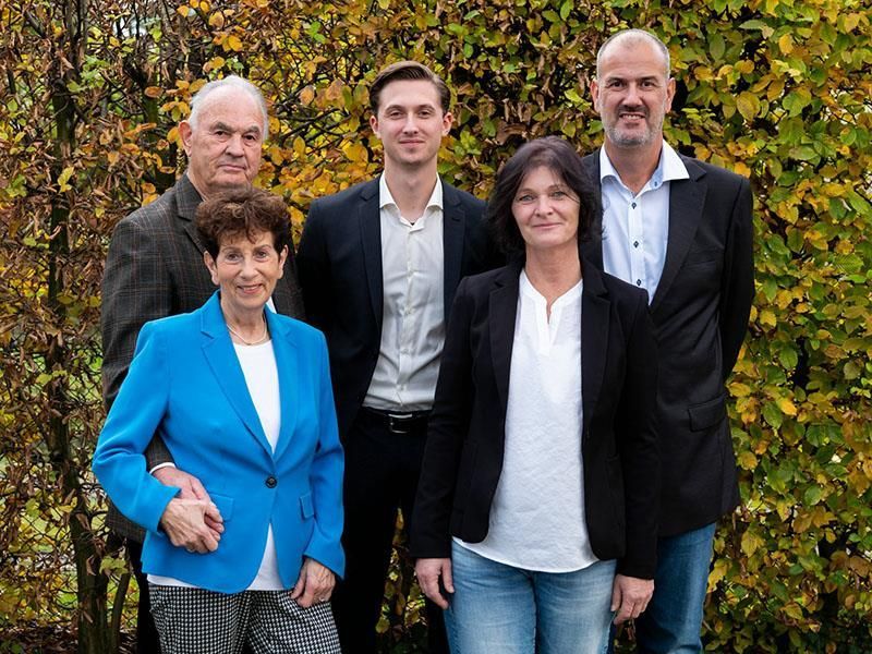 Eine Gruppe von Menschen steht nebeneinander vor einem Busch.