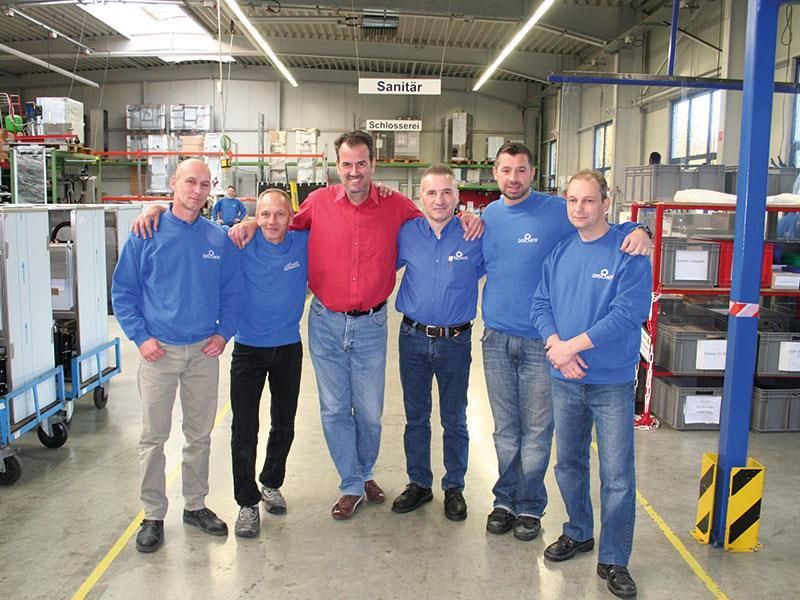 Eine Gruppe von Männern posiert für ein Foto in einem Lagerhaus mit einem Schild über ihnen, auf dem Service steht