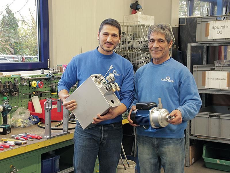 Zwei Männer in blauen Hemden halten eine Maschine in einer Werkstatt